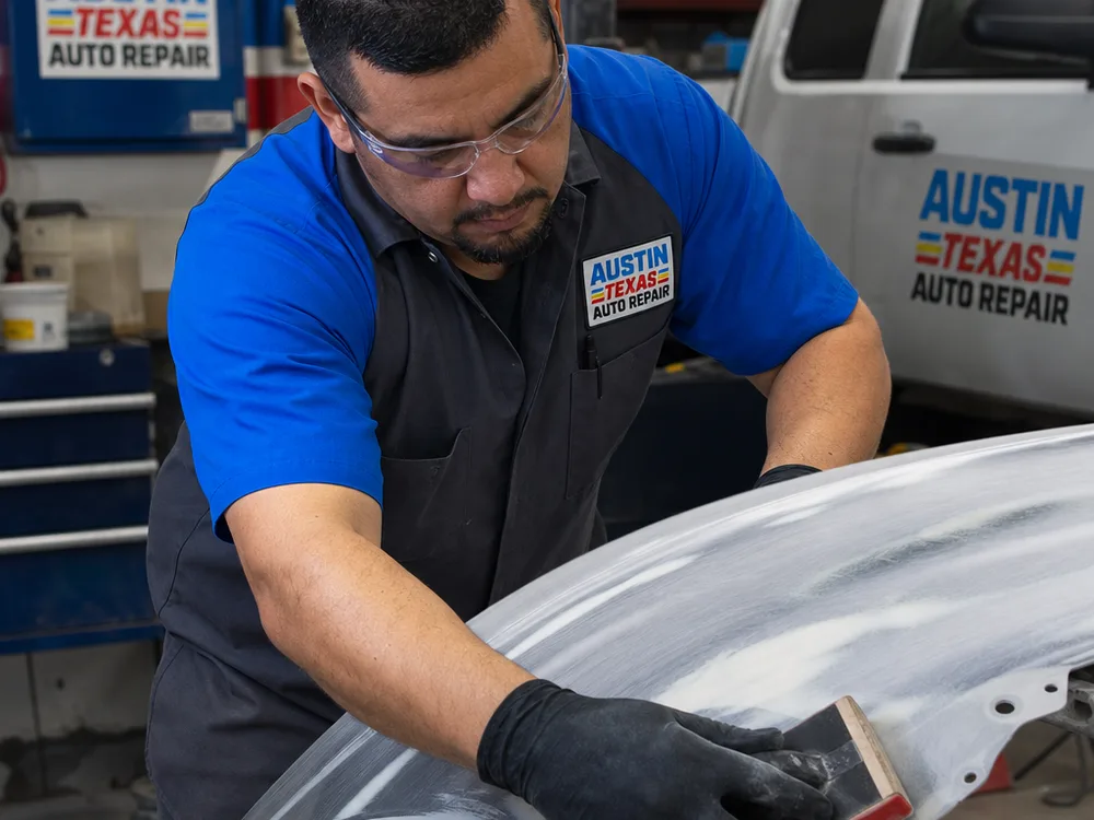 Technician block-sanding a primed classic-car fender with guide coat visible before paint